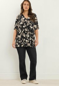 Sort blomsterbluse med korte ærmer og V-hals, parret med mørke denimjeans. Blusen har et løst, indsamlet design.