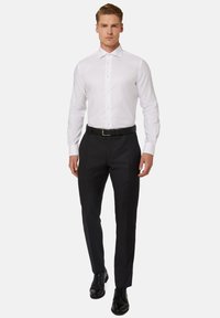 Camicetta bianca a maniche lunghe con chiusura a bottoni, abbinata a pantaloni neri su misura e scarpe eleganti nere. L'outfit appare formale e aderente.