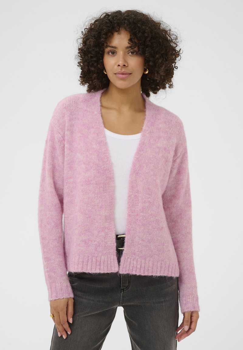 Cardigan rosa chiaro lavorato a maglia con una texture morbida, apertura frontale e orlo a coste. Abbinato a una maglietta bianca e jeans scuri.