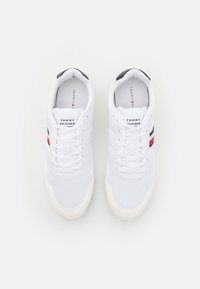 Białe sneakersy z siateczkowym i syntetycznym wierzchem, z navy i czerwonymi paskami, sznurowaniem oraz metką z logo na języku. Płaska podeszwa.