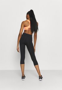 Sportbeha in neonoranje met racerback-design; zwarte capri leggings; textuurstof; sport sneakers met zwarte en witte accenten.