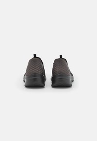Zapatos negros sin cordones con un tejido gris texturizado en la parte superior y suela de goma negra. Incluyen un talón acolchado y una lengüeta trasera para facilitar su uso.