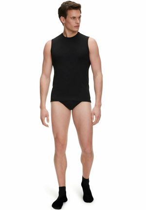 Schwarzes ärmelloses Herrenunterhemd aus einem glatten Stoff, mit einem runden Halsausschnitt und einer taillierten Passform. Getragen mit schwarzen Unterhosen und Knöchelsocken.
