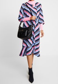 Abito colorato con strisce diagonali blu, rosa e marrone, caratterizzato da una vestibilità ampia, maniche corte e una cintura legata in vita. Una borsa a spalla nera completa il look.