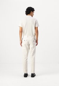 Polo shirt blanc à manches courtes avec un motif texturé ; pantalon beige ; vue arrière montrant deux poches, détails visibles de la taille et poignets retroussés.