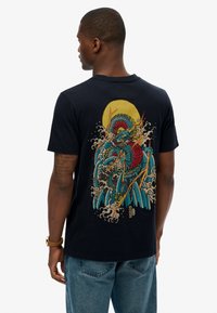 Navy katoenen T-shirt met een kleurrijke afbeelding van een draak tussen golven, met gele accenten en een grote zon op de achtergrond.