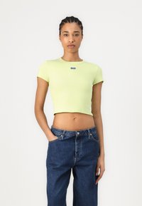 Vaaleanvihreä ribattu lyhythihainen crop-top, jossa on pyöreä kaula-aukko ja pieni sininen logoyksityiskohta. Yhdistetty tummansinisisiin leveälahkeisiin farkkuihin.