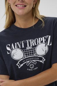 Tamsiai mėlynas marškinėliai su baltu dizainu, vaizduojančiu teniso raketes, tekstu "SAINT TROPEZ NY. RACQUET CLUB" ir minkšta medvilnės tekstūra.