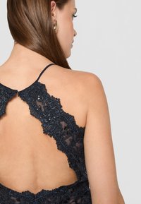 Tengerészkék csipke ruha bonyolult hímzett részletekkel és gyöngy díszítéssel. Mélyen dekoltált hátrésze és vékony pántjai fokozzák a finom dizájnt.