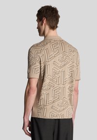 Polo shirt beige a maniche corte con un motivo geometrico testurizzato, dotato di un colletto classico e un orlo dritto. Tessuto a maglia morbido.