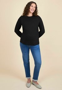 Camisetta nera a maniche lunghe abbinata a jeans blu con orlo arrotolato e ballerine grigie chiare. Tessuto morbido, vestibilità rilassata e design semplice.