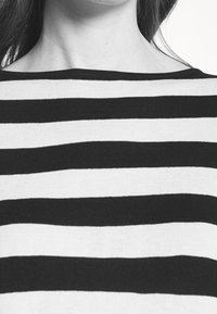 Sweter w paski charakteryzuje się szerokimi czarno-białymi poziomymi pasami. Ma miękką teksturę oraz dekolt łódka i luźny fason.
