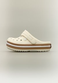 Μπεζ Crocs clog με οπές αερισμού, ρυθμιζόμενο λουράκι στη φτέρνα και πλατφόρμα με ρίγες καφέ και λευκού χρώματος σε απλό φόντο.