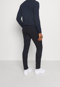 Navy longsleeve shirt gecombineerd met slim-fit navy broek en witte sneakers. Kenmerken zijn een ronde hals en ribgebreide manchetten.