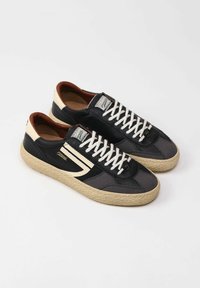 Sneaker nera e grigia con pelle texturizzata e mesh, dotata di una suola intermedia in juta intrecciata, lacci bianchi e dettagli crema sul tallone e sulla linguetta.