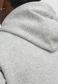 Sudadera gris con un material suave y texturizado y una capucha grande y redondeada. Se aprecian detalles de costura que enfatizan el diseño casual.