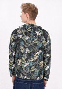 Giacca con cappuccio caratterizzata da uno sfondo nero con un motivo di foglie tropicali verdi e blu, realizzata in tessuto leggero con una superficie liscia.