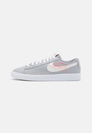 Lavtop grå Nike-sneaker med hvid sål, hvide snørebånd og stort hvidt og rødt Nike-logo på siden.