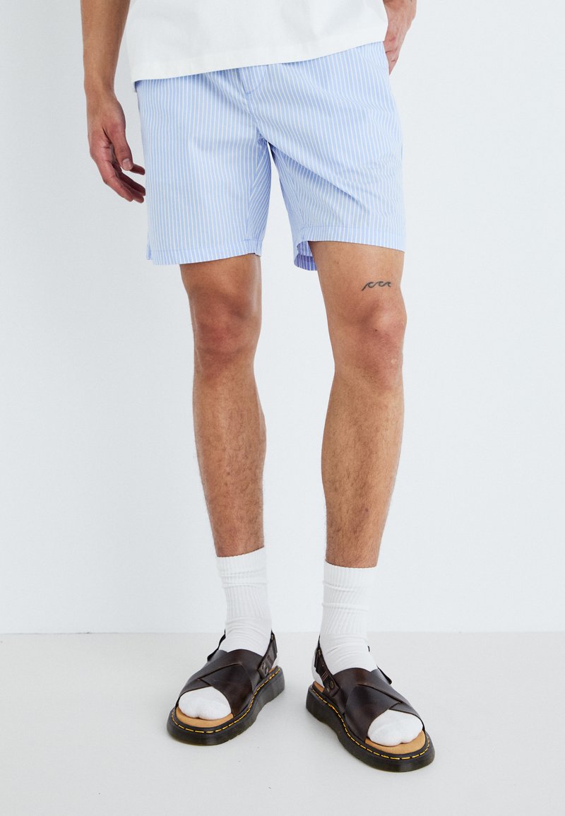 Lichtblauwe gestreepte shorts van stof, met een relaxte pasvorm en zijzakken, gecombineerd met witte sokken en donkere sandalen.