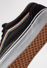 Svart kanvas sneakers med et regnbue-stripe design. Har hvite snørebånd, gummisåle og teksturert beige yttersåle med diamantmønster.