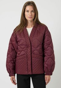 Burgundská prošívaná bunda s výstřihem do V, oversized silueta, geometrický vzor a přední kapsy; má bohaté rukávy a hladkou texturu látky.