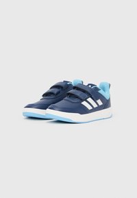 Tmavě modré tenisky se světle modrými akcenty, suchými zipy, bílým logem se třemi pruhy, strukturovaným syntetickým svrškem a bílou gumovou podrážkou.