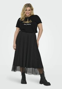 Svart t-shirt med guldtryck som säger "God Jul", kombinerad med en svart, plisserad, ankellång kjol och svarta snörstövlar.