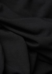 Schwarzer Stoff zeigt eine weiche, glatte Textur mit leichtem Glanz. Enthält zerknitterte Bereiche, die seinen Fall und das leichte Aussehen betonen.