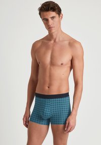 Blauwe boxershorts met patroon en een zwarte tailleband; heeft geometrische vormen in een herhalend ontwerp; zachte stof, aangesloten snit.