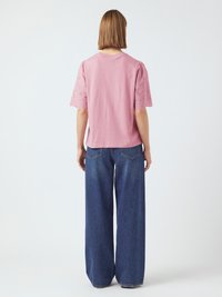 T-shirt en coton rose à manches courtes bouffantes avec un détail en dentelle, associé à un jean bleu foncé ample avec des poches arrière.