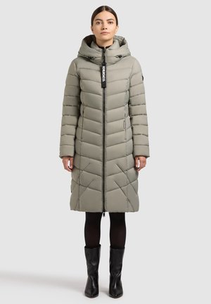 Kurtka puchowa w jasno szarym kolorze z kapturem. Ma zamek błyskawiczny z przodu, dwie boczne kieszenie i pikowany wzór. Noszona z czarnymi, sięgającymi kolan kozakami.