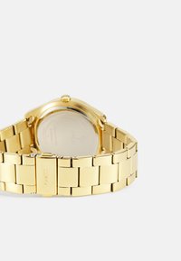 Goldfarbene Metalluhr mit einem verbundenen Armbanddesign. Runder Gehäuse mit glattem Lünette, klarem Glas und eingraviertem Logo der Marke auf der Rückseite.