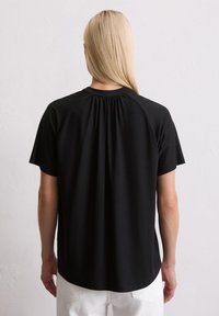 Schwarzes T-Shirt mit kurzen Ärmeln, das einen gerafften Rückenausschnitt aufweist. Es besteht aus weichem Stoff mit glatter Textur und bietet eine entspannte Passform.
