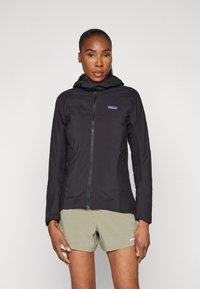 Black hooded jacket with a full zipper, mesh accents, and side pockets. Lightweight fabric and fitted shape, paired with olive shorts.