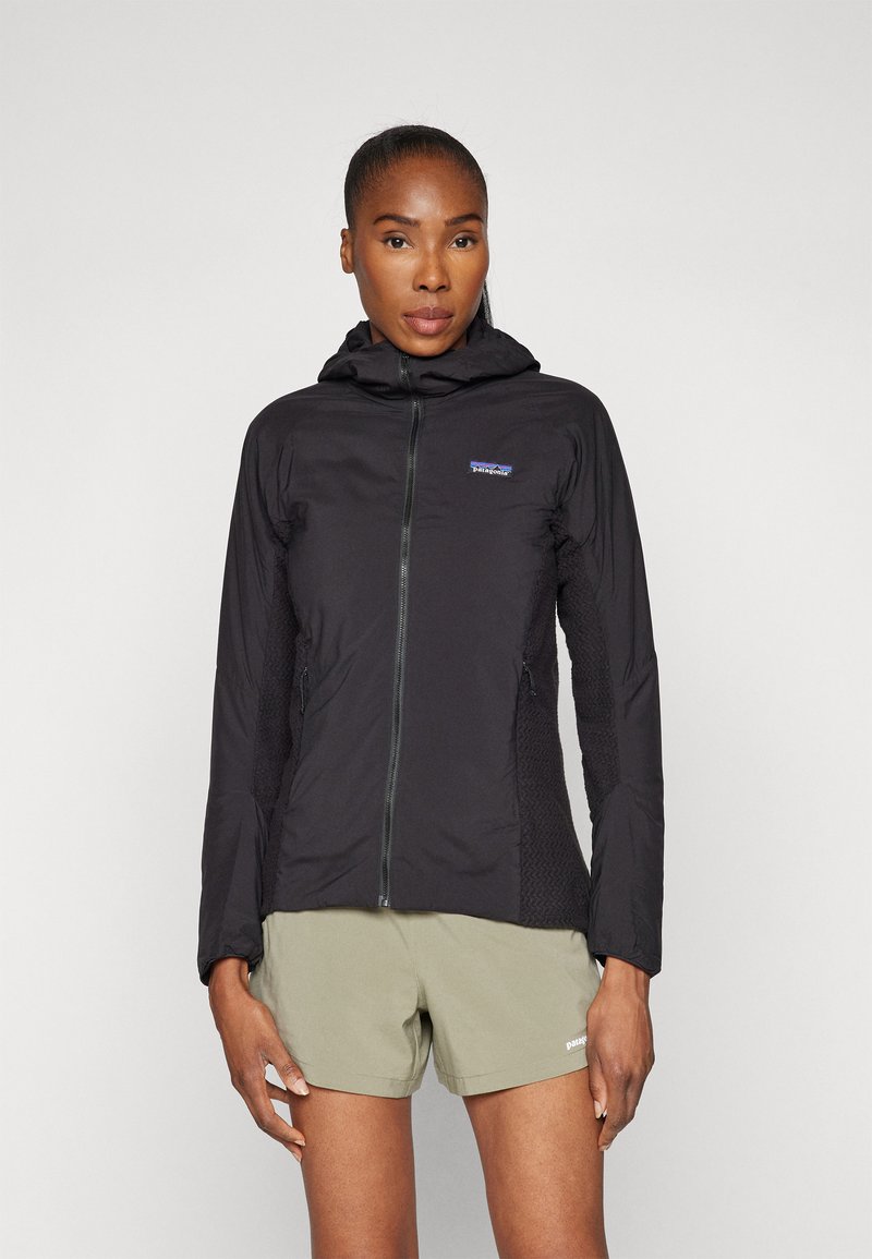 Black hooded jacket with a full zipper, mesh accents, and side pockets. Lightweight fabric and fitted shape, paired with olive shorts.