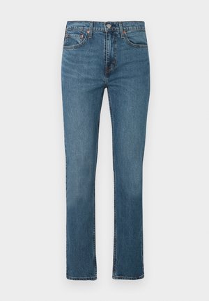 Stramme blå denimjeans med frontlommer, beltehemper og knappelukking på en ensfarget hvit bakgrunn.