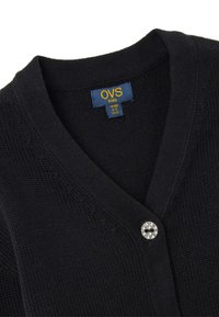 Schwarze gestrickte Strickjacke mit V-Ausschnitt, ausgestattet mit einem dekorativen silbernen Knopf. Das Größenetikett weist auf eine Eignung für Kinder im Alter von 4-5 Jahren hin.