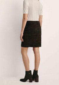 Kobieta w czarnej zamszowej mini spódnicy, białej bluzce z krótkim rękawem i czarnych botkach za kostkę na słupkowym obcasie, widoczna z tyłu.