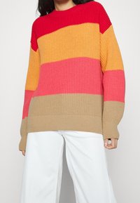 Mehrfarbiger Strickpullover mit horizontalen Streifen in Rot, Orange, Pink und Beige, lockerer Passform sowie geripptem Halsausschnitt und Bündchen.