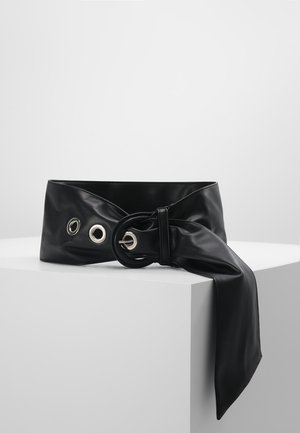 Sort bredt læderbælte med stor cirkulær spænde og overdimensionerede sølvøjer, bundet med en lang rem, der hænger ned.