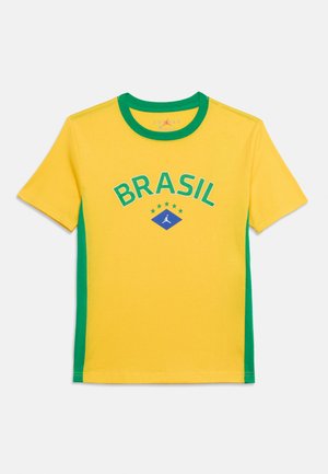 Gul og grøn shortærmet sportstrøje med teksten "BRASIL", fem stjerner og et blåt diamantlogo med en hvid silhuet af en basketballspiller.
