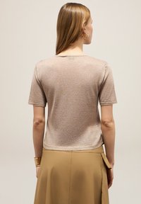 Korte mouwen, lichtbeige gebreide trui met een subtiele glans. Kenmerkt zich door een ronde halslijn en een iets verkorte zoom.