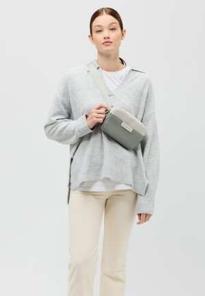 Maglione grigio lavorato a maglia con scollo a V, pantaloni crema e una borsa a tracolla morbida grigia e grigia chiara. La borsa ha una forma rettangolare e un'etichetta con il logo.