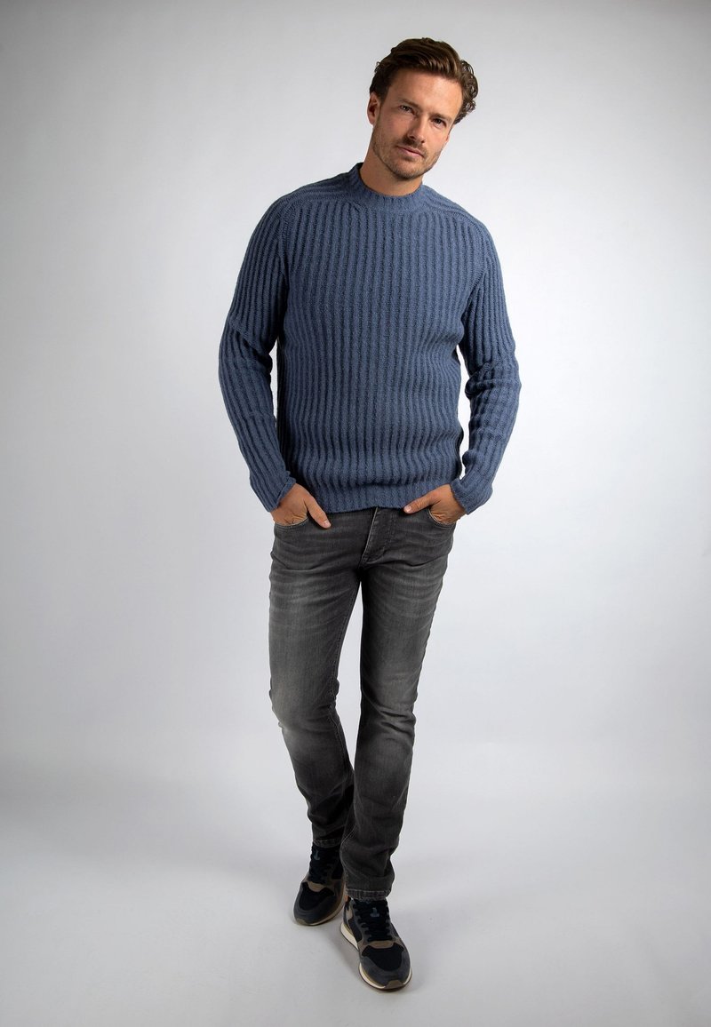Blauwe ribgebreide sweater met een ronde hals, gecombineerd met grijze jeans en donkere sneakers. Zachte textuur met verticale lijnen en lange mouwen.