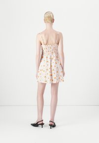 Rochie albă cu un model floral portocaliu și verde, cu top smockat, bretele subțiri, fustă evazată, asortată cu pantofi cu toc negri.
