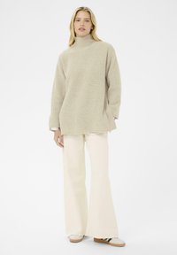 Maglioncino beige a collo alto con costine, taglio oversize, abbinato a pantaloni larghi color crema e sneakers bianche con dettagli neri. Design semplice e testurizzato.