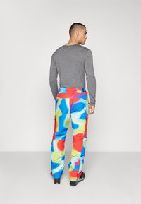 Pantalones de esquí coloridos con una mezcla de patrones abstractos en azul, rojo y amarillo, fabricados con un tejido duradero, con cintura ajustable y bolsillos.