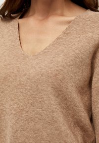 Brun strikket sweater med V-hals, blød tekstur og afslappet pasform. Stoffet synes let og let tekstureret med et afslappet design.