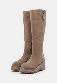 Brown suede knee-high boots with a chunky wedge sole, side zipper, and a circular tag accent. Features contrast stitching along the sole.