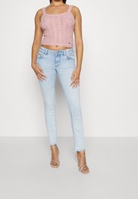 Světle růžový pletený crop top s širokými ramínky, spárovaný s džínami v světle modré barvě s úzkým střihem. Sandály mají řemínky kolem kotníků a tenký podpatek.